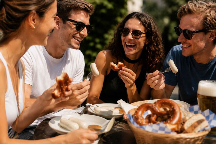 A group of people enjoying a meal outdoors with pretzels, sausages, and beer. 2