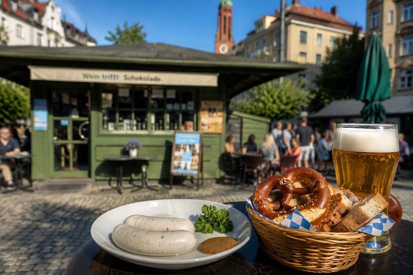 A plate of sausages, pretzels, and a glass of beer on a table with a green awning in the background. 4