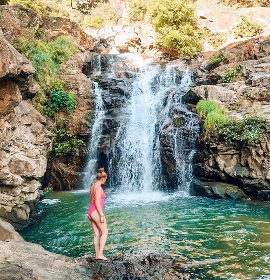 A woman in a pink swimsuit standing at the edge of a waterfall. 5