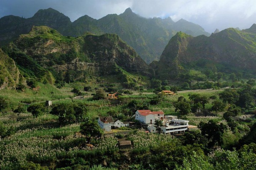 A rural landscape with a house surrounded by lush greenery and mountains in the background. 4