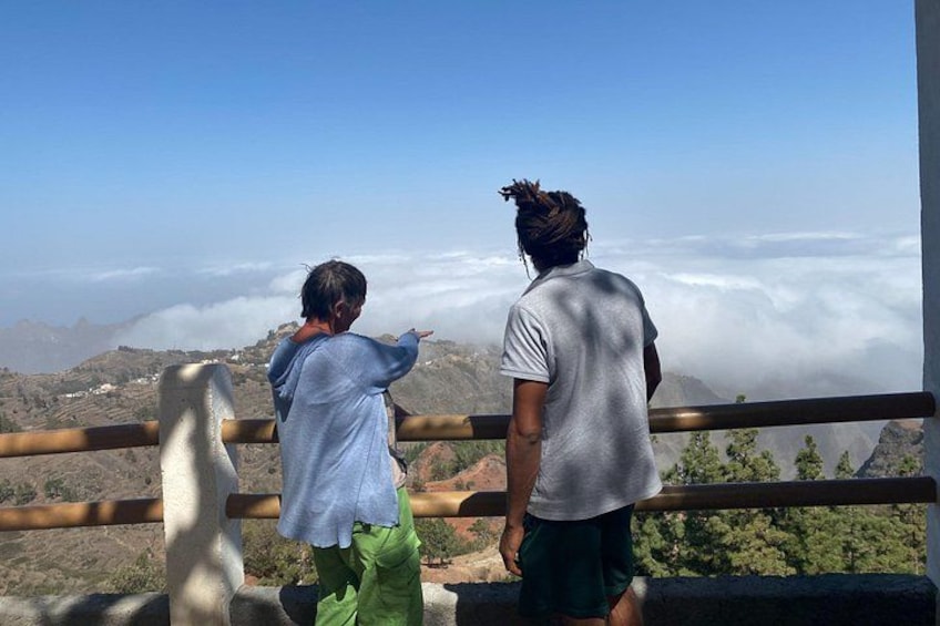 Two people standing on a balcony overlooking a mountainous landscape with clouds below. 2