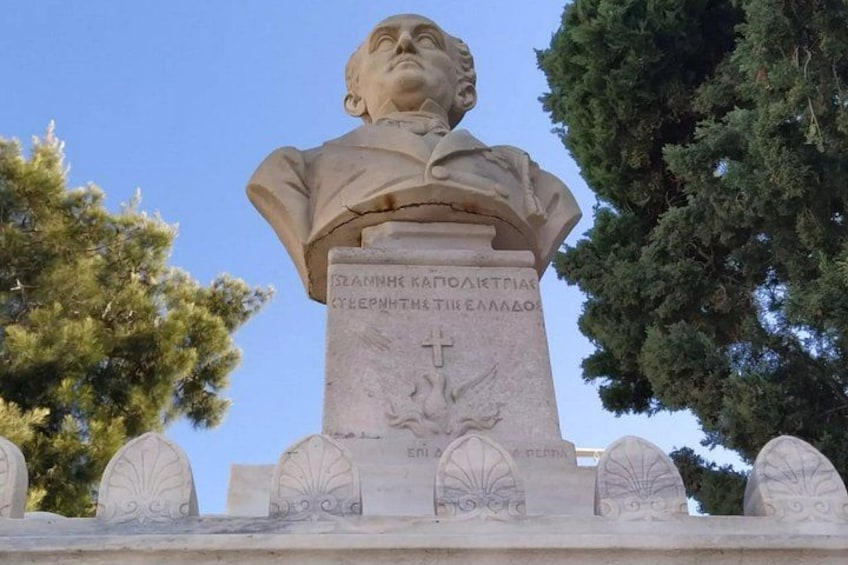A bust monument with inscriptions, surrounded by trees and a clear sky. 1