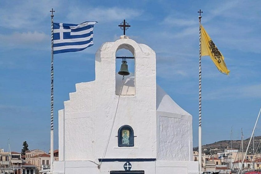 A white church with a bell tower, Greek flag, and a yellow flag. 2