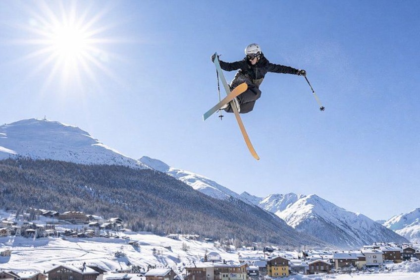 A skier in mid-air performing a jump with skis, a clear sky, and snow-covered mountains in the background. 3