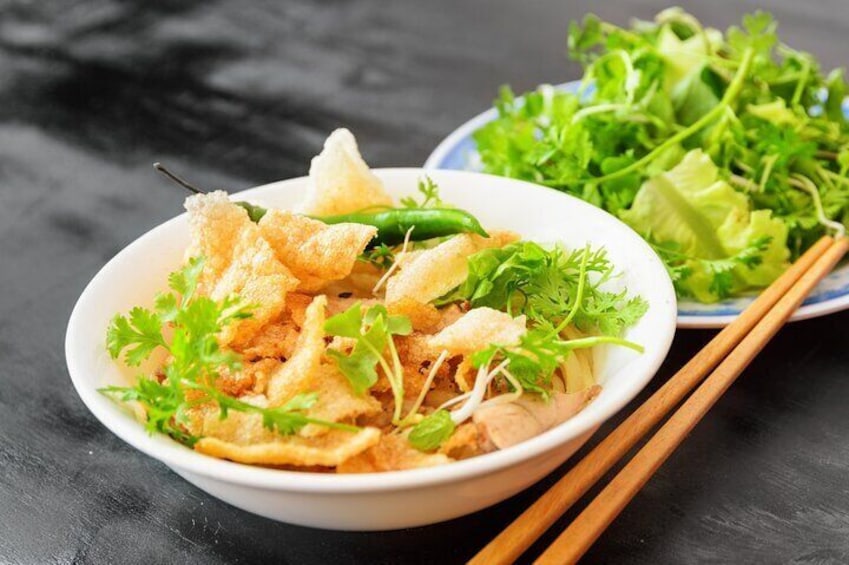 A bowl of fried wonton noodles garnished with cilantro and green onions, accompanied by a side salad and chopsticks. 5