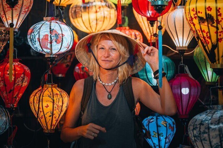 A person in a dark tank top and wide-brimmed hat surrounded by colorful lanterns. 4