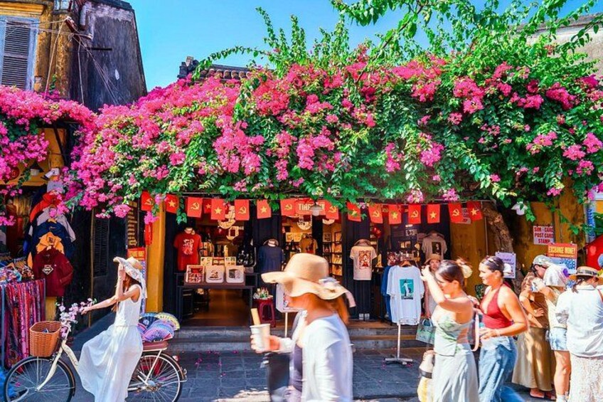 A street market with people shopping, a bicycle, and a building with red decorations. 2