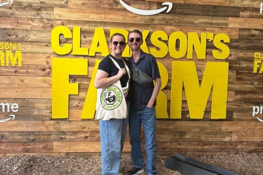Dos personas de pie frente a una pared de madera con letras amarillas grandes que deletrean 'CLADSON'S FARM'. 4