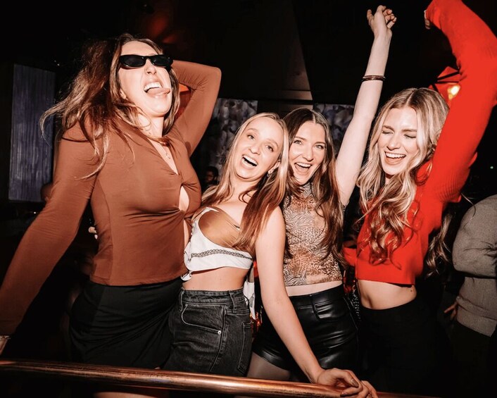 A group of people at a social event, possibly a party or club, with one person raising their arm in the air. 2