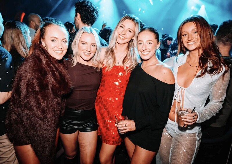 A group of people at a social event with dim lighting and a crowd in the background. 5