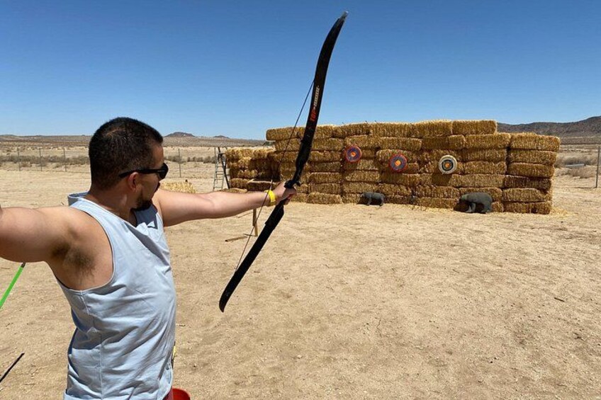 A person aiming a bow at a target with arrows in a desert setting. 3