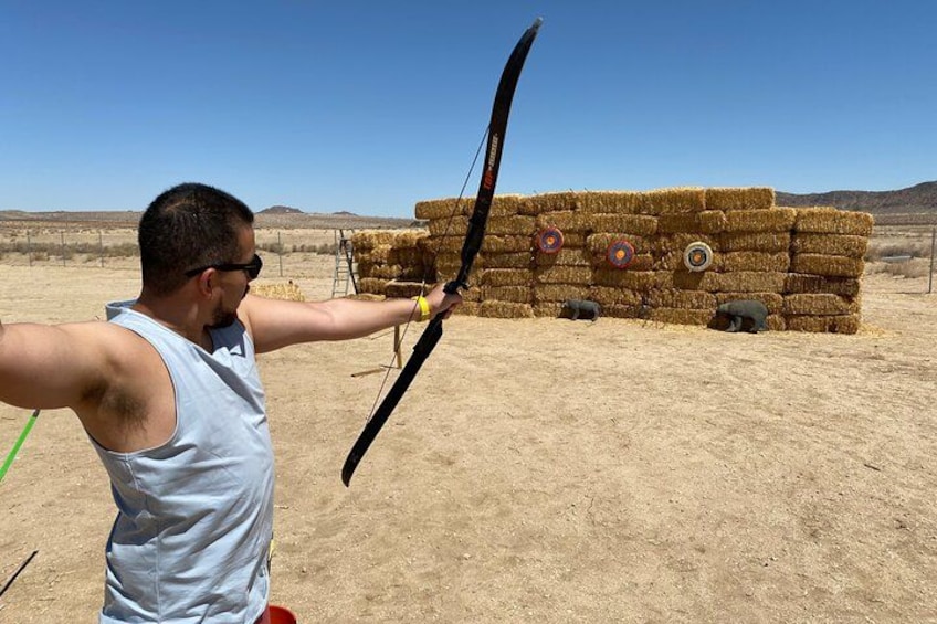 A person aiming a bow at a target in an outdoor setting. 3