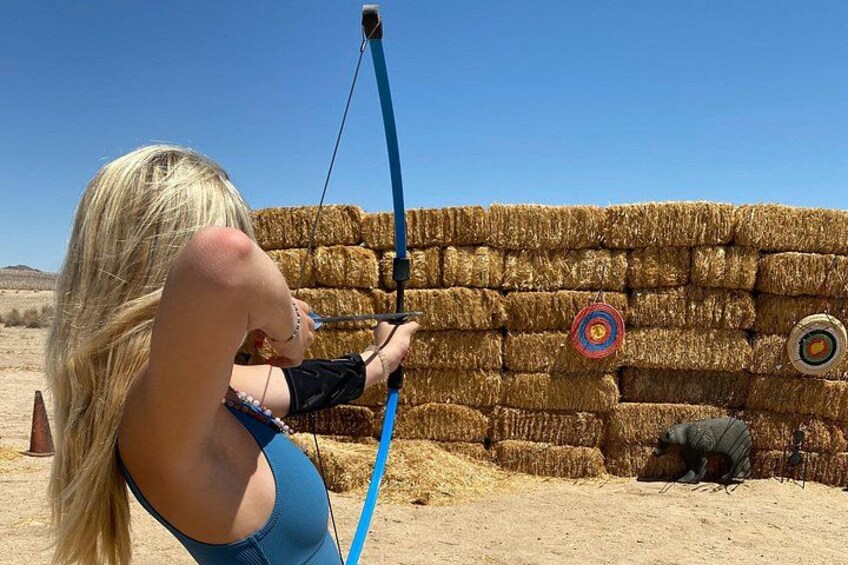 A person aiming a bow at a target with hay bales in the background. 4