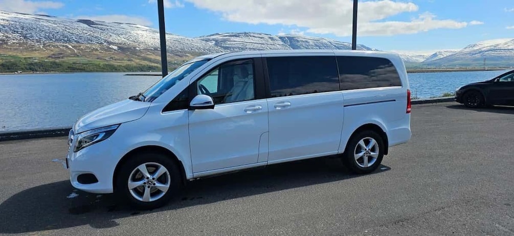 A white van parked by a lake with mountains in the background. 2