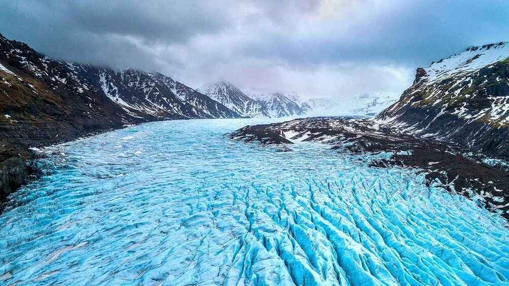 A glacier with a blue hue, surrounded by mountains and a cloudy sky. 1