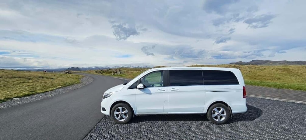A white van parked on a road with a rural landscape in the background. 5
