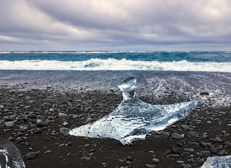 A piece of ice sculpture on a rocky beach with waves in the background. 5