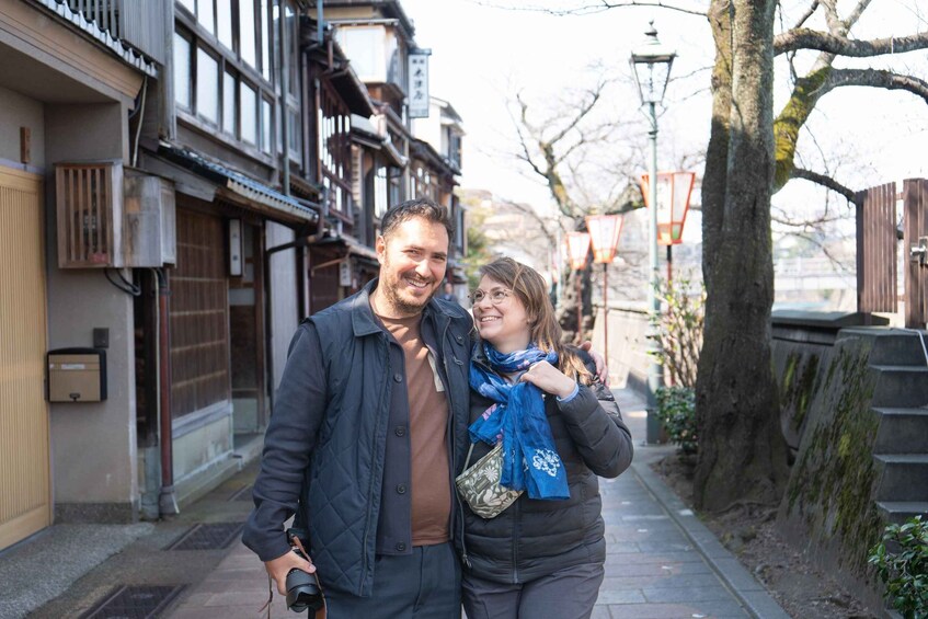 A couple walking on a tree-lined street with traditional buildings. 5