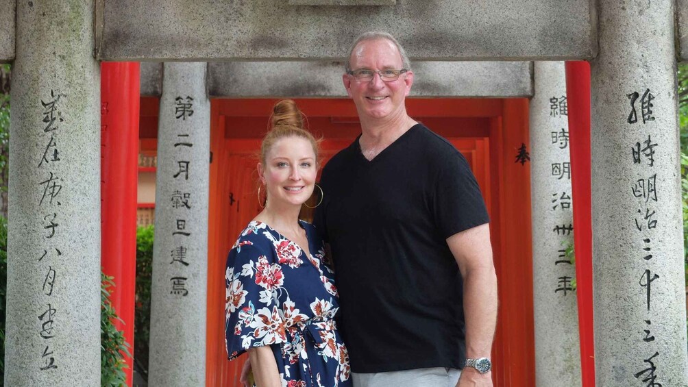 Two people standing in front of a building with red doors and stone pillars with Japanese characters. 5