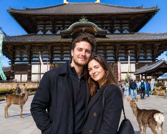 A couple in front of a traditional Japanese building with deer in the background. 1