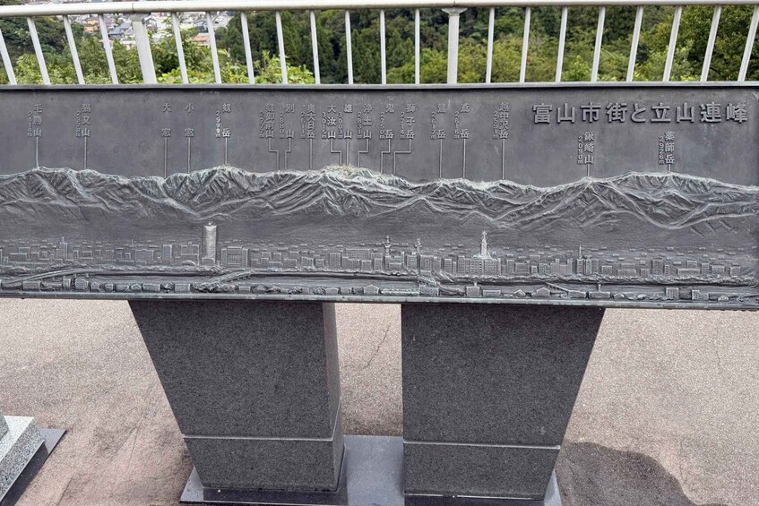 A detailed stone plaque with a mountain range and cityscape engraving, mounted on a metal frame. 5