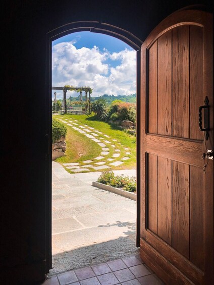 An open wooden door leading to a garden with a stone pathway, greenery, and a pergola. 3