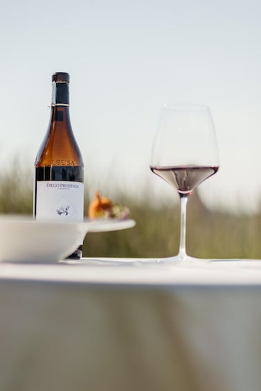 A bottle of wine and a glass on a table outdoors. 1