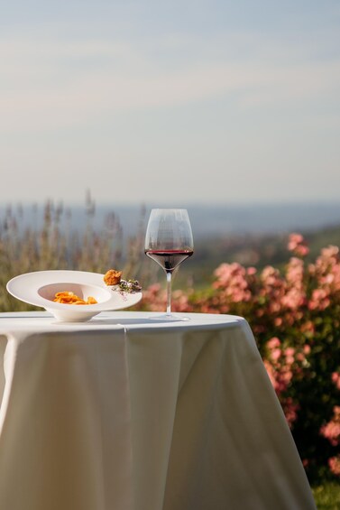 A table with a white tablecloth, a glass of red wine, and a plate of food with a small piece of meat and vegetables. 4