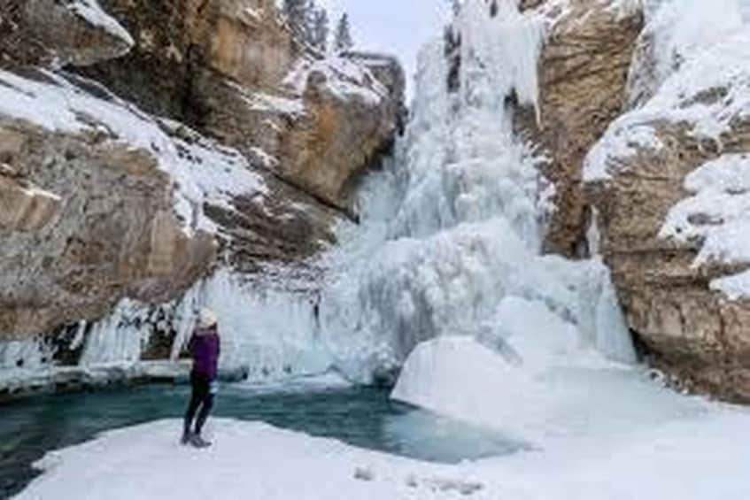 A person standing in a snow-covered canyon with a frozen waterfall. 2