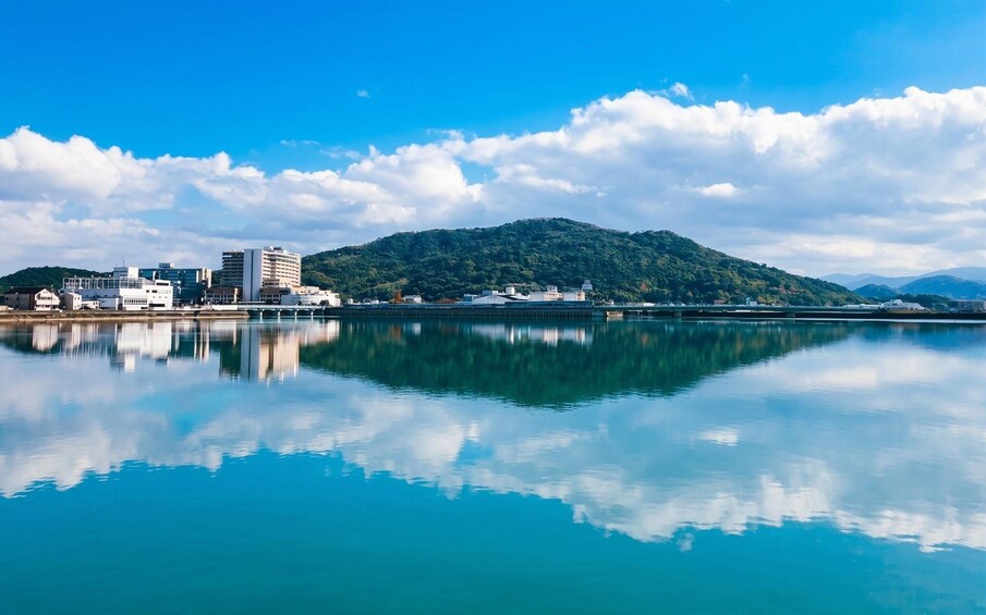 A calm lake with a cityscape and a hill in the background. 5