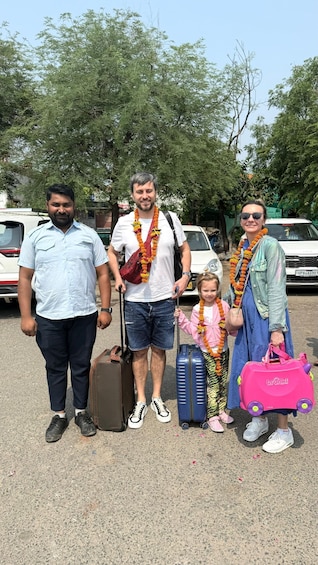 A family with luggage, wearing garlands, and standing in a parking lot. 5