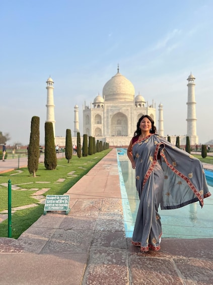 A person in a grey saree with red and gold embroidery standing in front of the Taj Mahal. 1