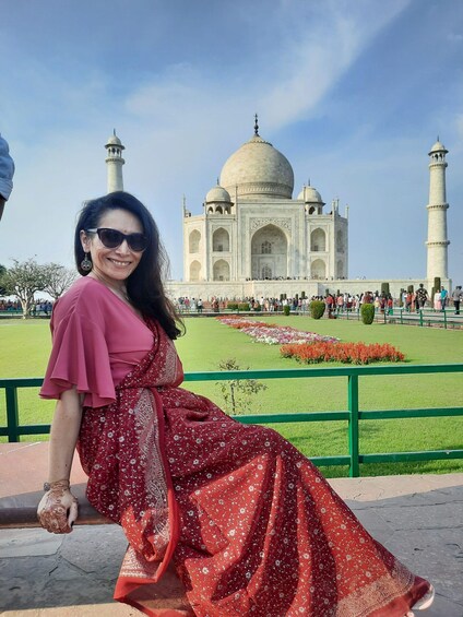 A woman in a red dress sitting on a bench with the Taj Mahal in the background. 3