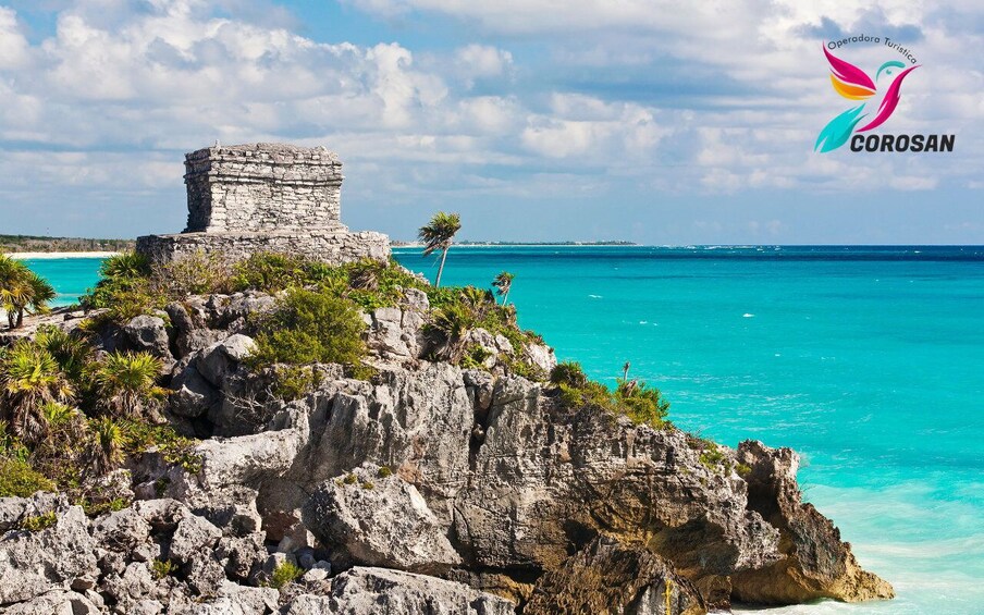 A stone ruin on a cliff overlooking turquoise waters. 1