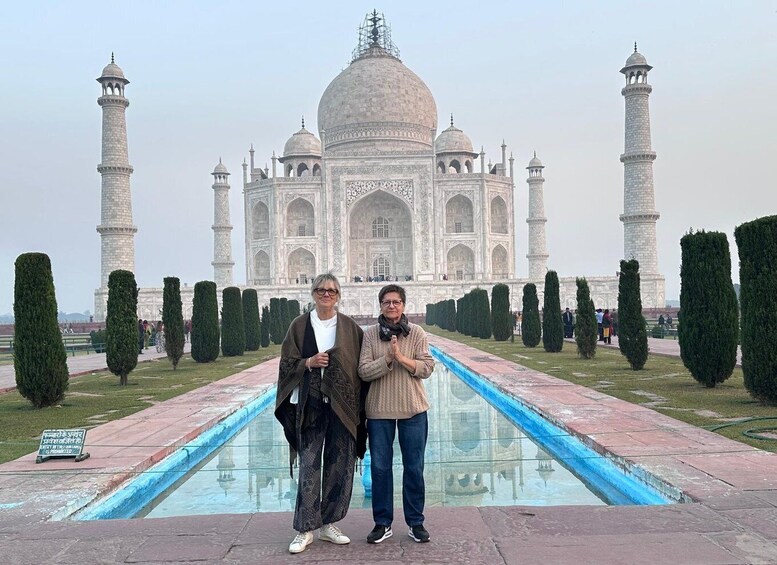 Two people standing in front of the Taj Mahal with a pool and trimmed hedges. 1