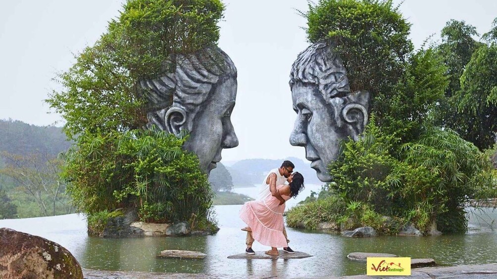 Una pareja se abraza frente a una escultura con dos rostros. 5