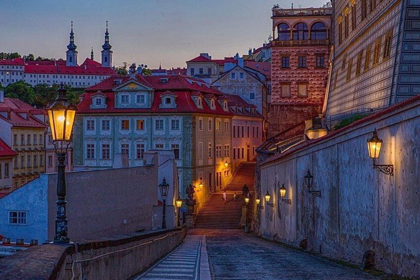 A historic street with buildings, a staircase, and street lamps. 4