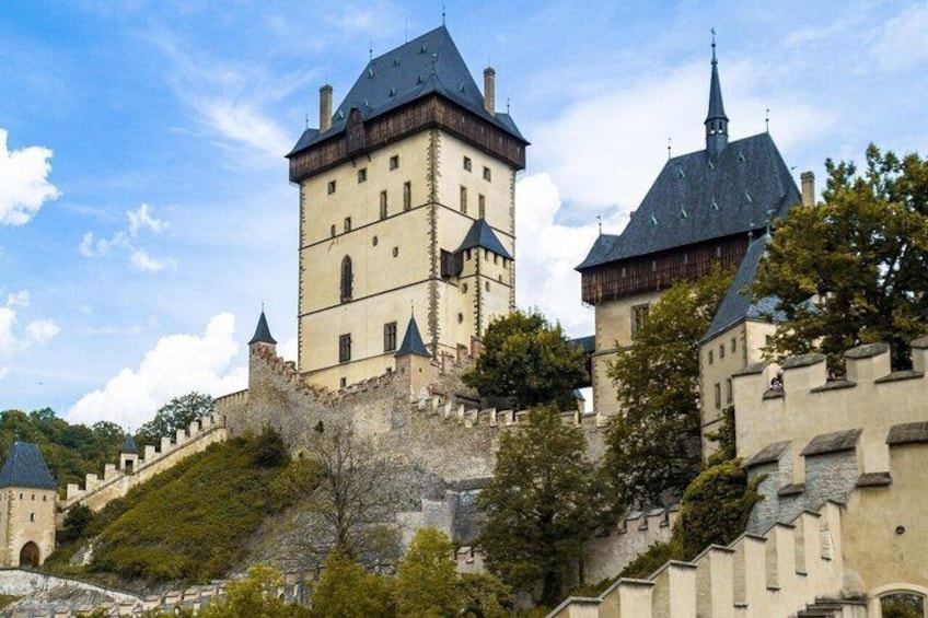 A historic castle with multiple towers, a stone wall, and lush greenery. 1