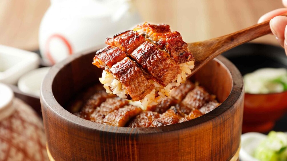 A wooden bowl filled with a dish of glazed meat and rice. 2