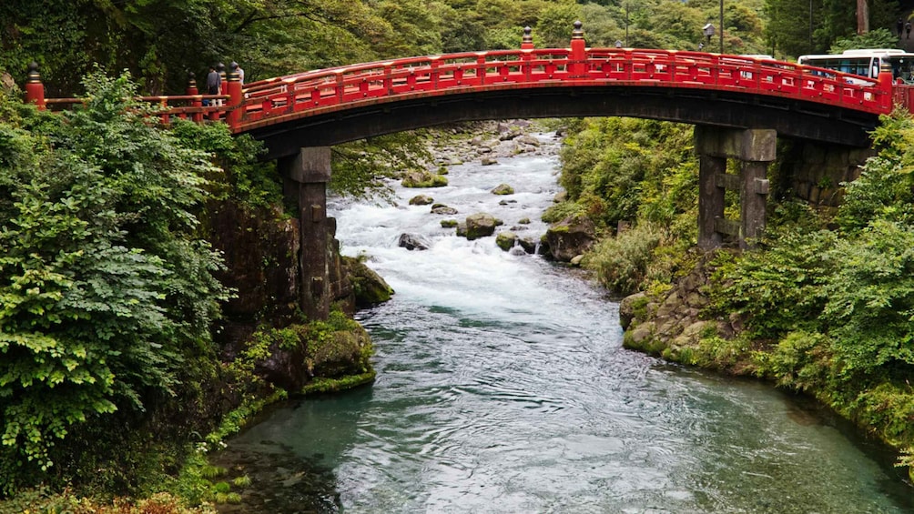 A red bridge over a flowing river surrounded by lush greenery. 1