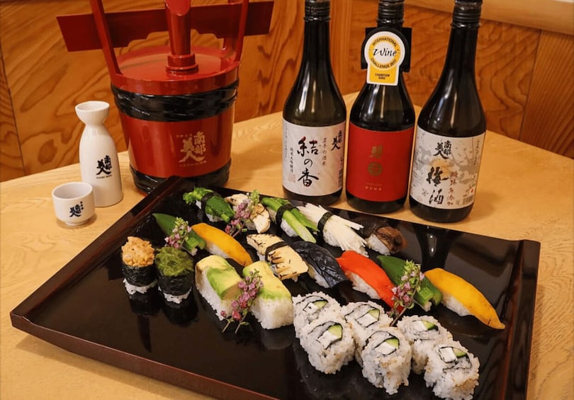 A tray of sushi with three bottles of wine and a red container on a wooden table. 2