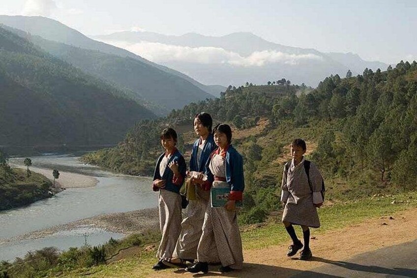 A group of people standing on a road with a river and mountains in the background. 5