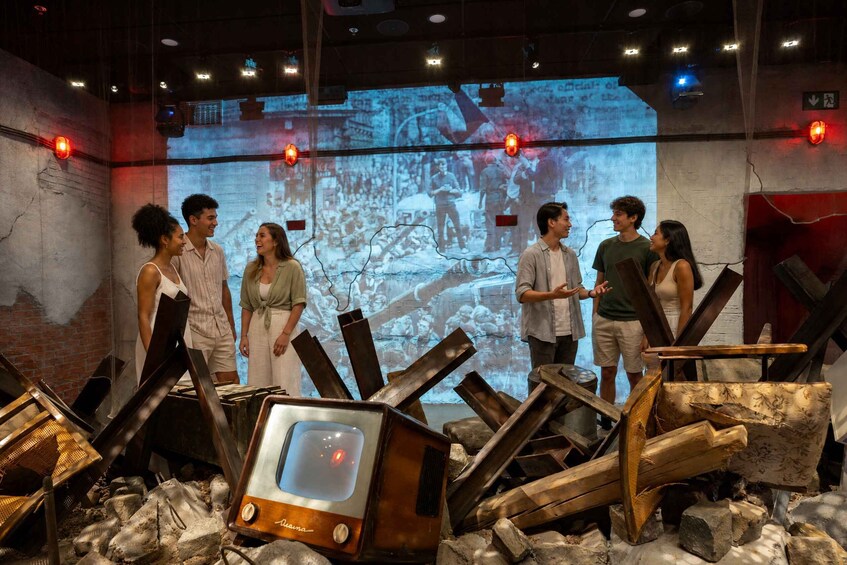 A group of people in an art installation with a television set surrounded by debris and a projected image on the wall. 5