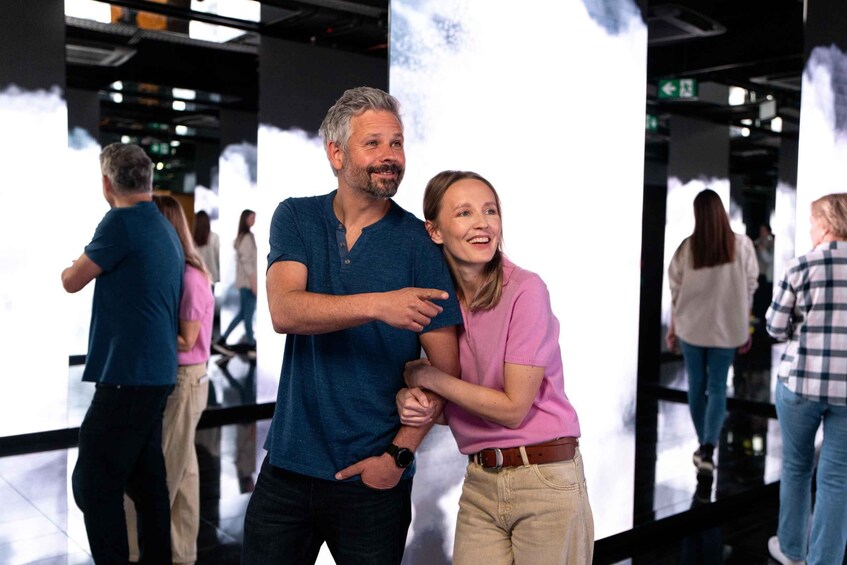 A man and woman embracing in a public indoor space with reflective floors and a large screen displaying a white image. 5