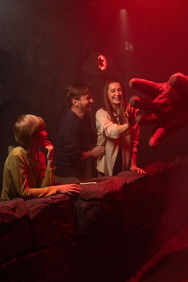 A group of people in a dimly lit room with red lighting, interacting with a large red stuffed animal. 3