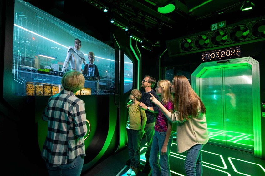 A group of people in a futuristic-themed room with digital displays and green lighting. 2