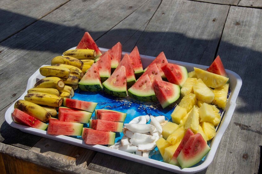 A tray of sliced fruits including watermelon, pineapple, and bananas on a wooden surface. 3