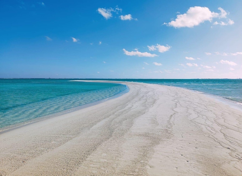 A wide, white sandy beach with clear turquoise water and a few scattered clouds in a clear blue sky. 1