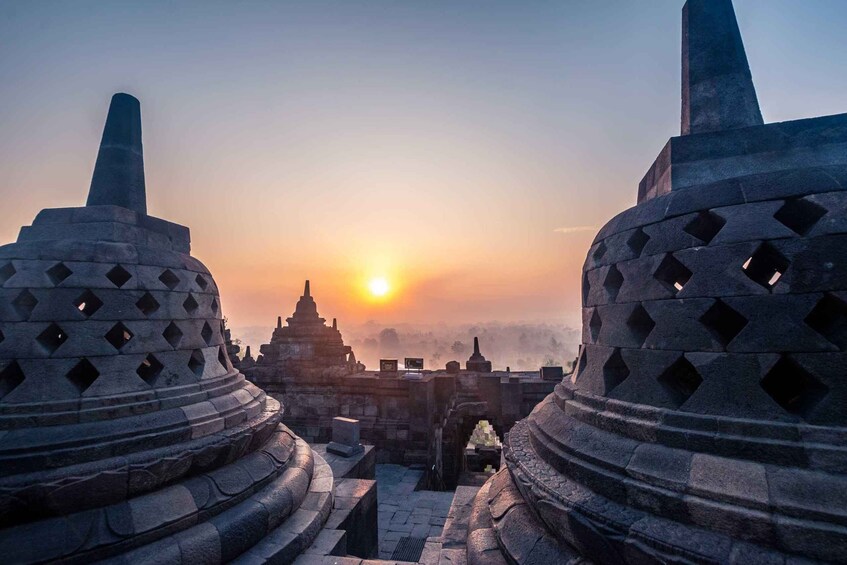 A temple complex with large stone structures and a sunset in the background. 1