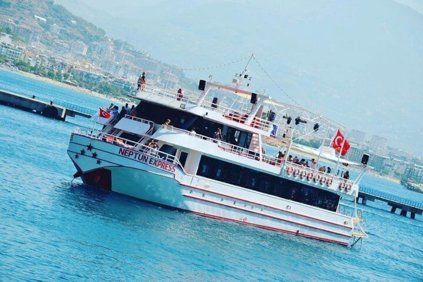 Un ferry Neptune Express con varios niveles y pasajeros, navegando sobre una masa de agua con un paisaje urbano al fondo. 4